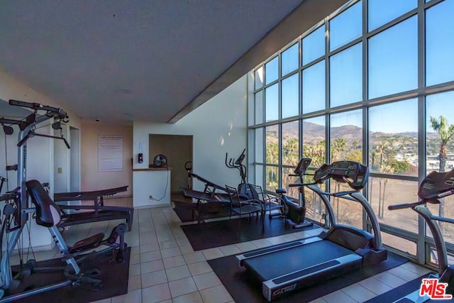 gym featuring tile patterned flooring, floor to ceiling windows, and a mountain view