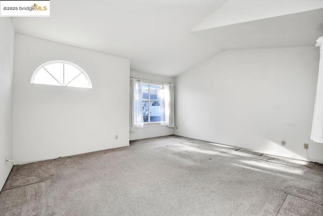 unfurnished room with a wealth of natural light, vaulted ceiling, and carpet