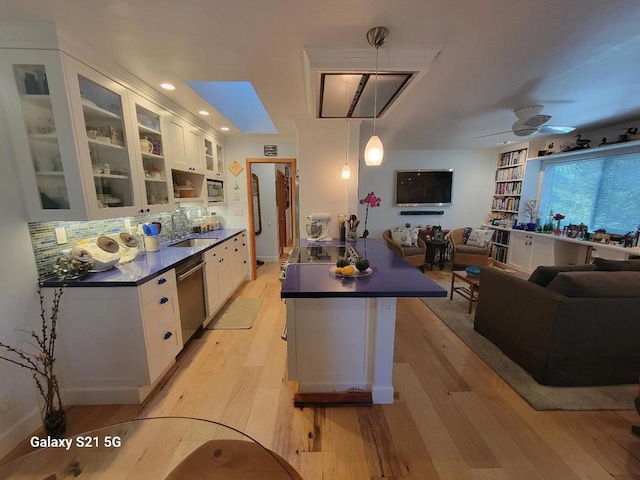 kitchen featuring sink, hanging light fixtures, light wood-type flooring, stainless steel dishwasher, and white cabinets