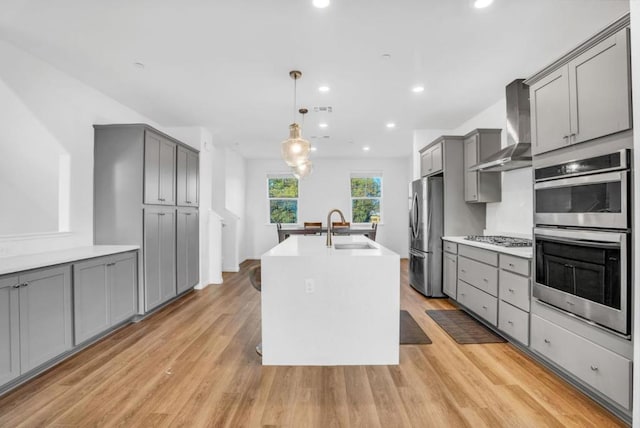 kitchen with gray cabinets, appliances with stainless steel finishes, pendant lighting, sink, and wall chimney range hood