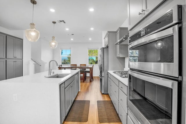 kitchen with sink, gray cabinetry, pendant lighting, stainless steel appliances, and a kitchen island with sink