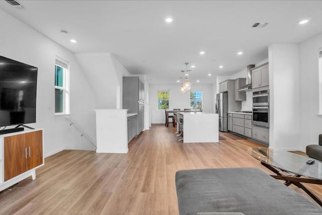 kitchen featuring a kitchen island, a breakfast bar, pendant lighting, appliances with stainless steel finishes, and gray cabinetry