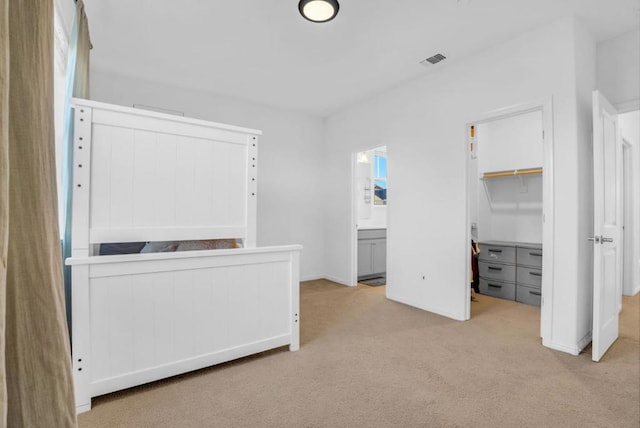 unfurnished bedroom featuring a walk in closet, light colored carpet, ensuite bath, and a closet