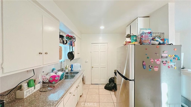 kitchen with light tile patterned flooring, stainless steel refrigerator, sink, white cabinets, and light stone counters