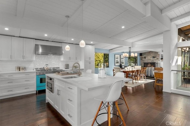 kitchen featuring sink, white cabinetry, an island with sink, decorative light fixtures, and wall chimney exhaust hood