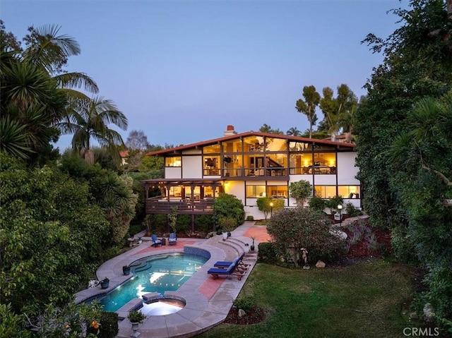 back house at dusk featuring a patio, a balcony, and a pool with hot tub