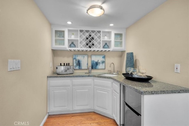 bar with white cabinetry, sink, light hardwood / wood-style flooring, and stone countertops