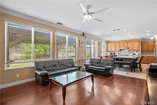 living room with ornamental molding, dark wood-type flooring, and ceiling fan