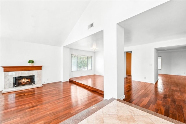 unfurnished living room with high vaulted ceiling, a tile fireplace, and light hardwood / wood-style floors