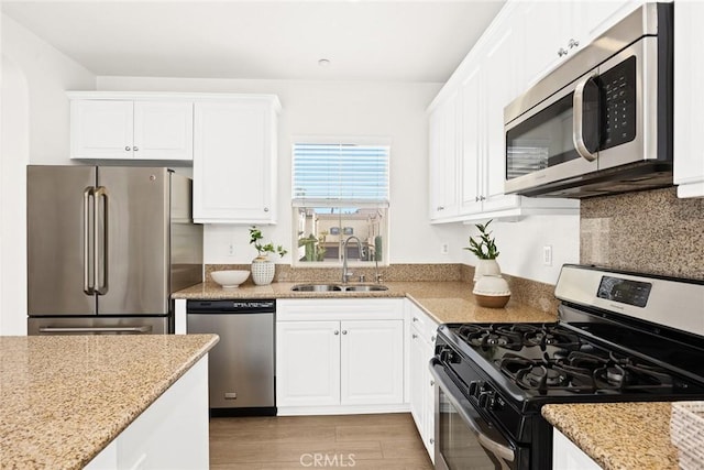 kitchen with sink, light stone counters, light wood-type flooring, stainless steel appliances, and white cabinets