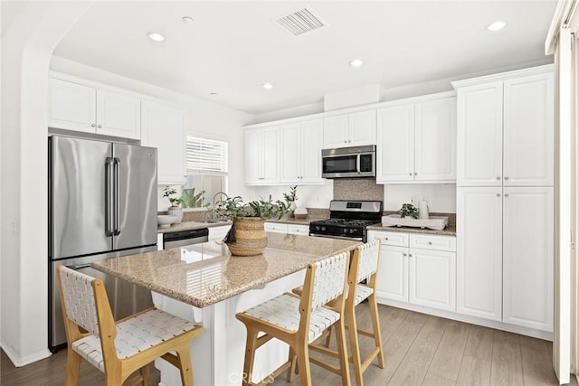 kitchen featuring white cabinetry, light stone countertops, a center island, and appliances with stainless steel finishes