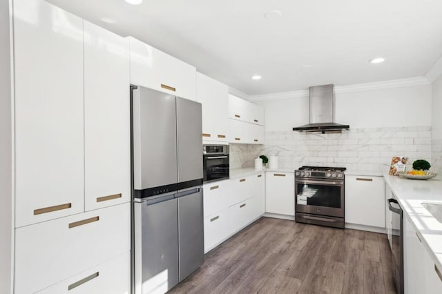 kitchen with white cabinetry, wood-type flooring, wall chimney range hood, stainless steel appliances, and backsplash