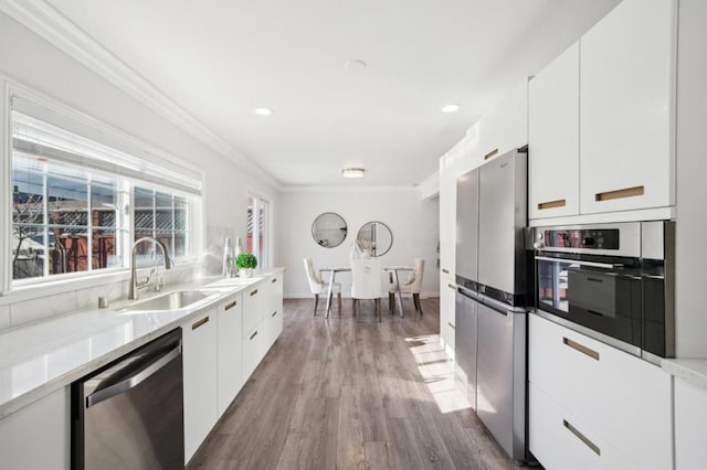 kitchen featuring sink, ornamental molding, appliances with stainless steel finishes, hardwood / wood-style floors, and white cabinets