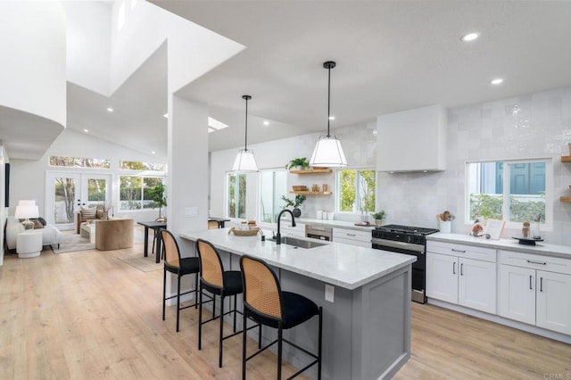 kitchen with sink, gas stove, tasteful backsplash, pendant lighting, and white cabinets