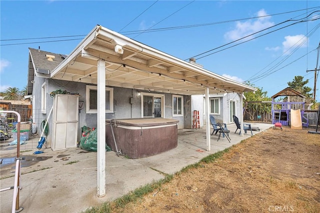 rear view of property with a patio area, a hot tub, and a playground