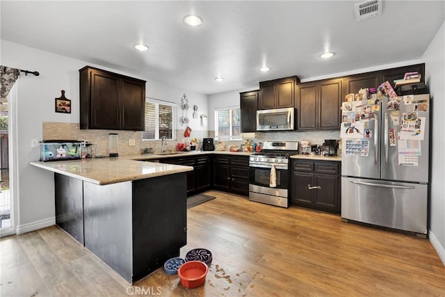 kitchen featuring sink, dark brown cabinetry, kitchen peninsula, stainless steel appliances, and light hardwood / wood-style flooring