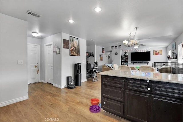 kitchen featuring light stone counters, ceiling fan, hanging light fixtures, and light wood-type flooring