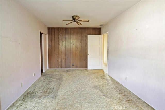 carpeted empty room with ceiling fan and wood walls