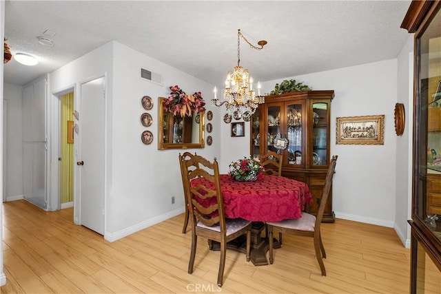 dining space with a textured ceiling, light hardwood / wood-style floors, and a chandelier