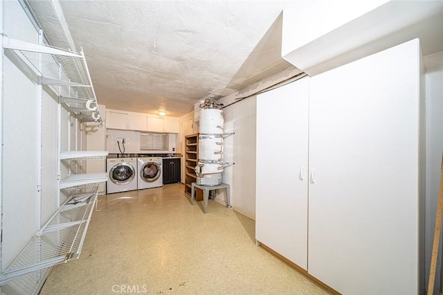 clothes washing area with strapped water heater and washer and clothes dryer