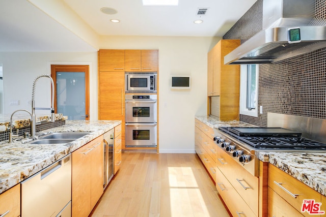 kitchen featuring sink, light wood-type flooring, light stone countertops, stainless steel appliances, and range hood