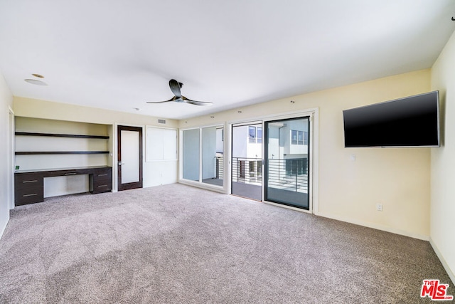 unfurnished living room featuring built in desk, ceiling fan, and carpet flooring