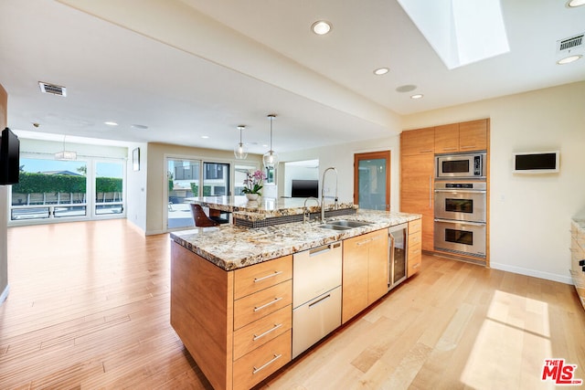 kitchen with sink, appliances with stainless steel finishes, a skylight, a spacious island, and light stone counters