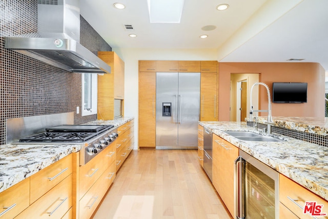 kitchen featuring wall chimney range hood, sink, light hardwood / wood-style flooring, appliances with stainless steel finishes, and wine cooler