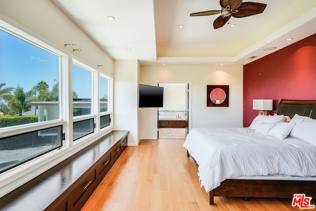 bedroom with multiple windows, a tray ceiling, light hardwood / wood-style floors, and ceiling fan