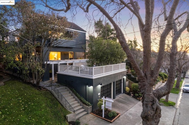 back house at dusk featuring a garage, a balcony, and a yard