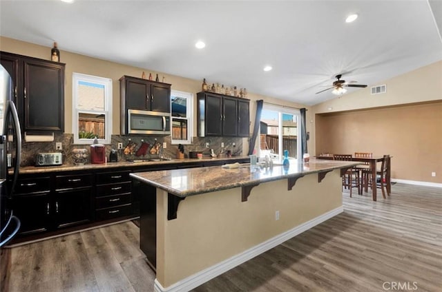 kitchen featuring a breakfast bar, lofted ceiling, a kitchen island with sink, stainless steel appliances, and light stone countertops