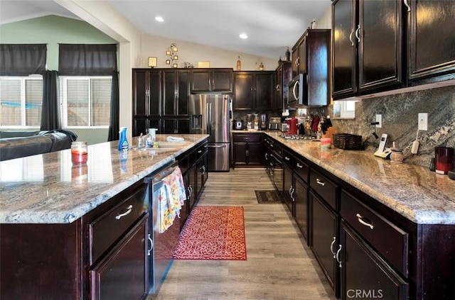 kitchen featuring vaulted ceiling, appliances with stainless steel finishes, backsplash, dark brown cabinetry, and light hardwood / wood-style flooring