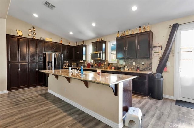 kitchen featuring lofted ceiling, a breakfast bar area, a kitchen island with sink, hardwood / wood-style floors, and light stone counters