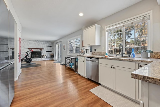 kitchen with sink, brick wall, stainless steel dishwasher, a healthy amount of sunlight, and white cabinets