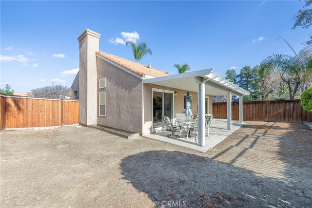 rear view of property with a tile roof, a chimney, stucco siding, a patio area, and a fenced backyard