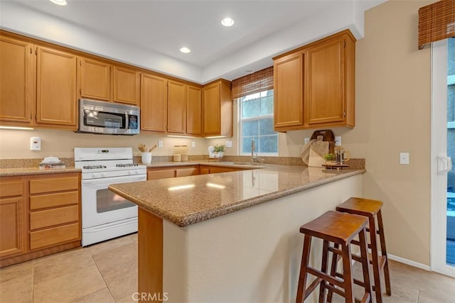 kitchen with white gas range, sink, light tile patterned floors, light stone counters, and kitchen peninsula