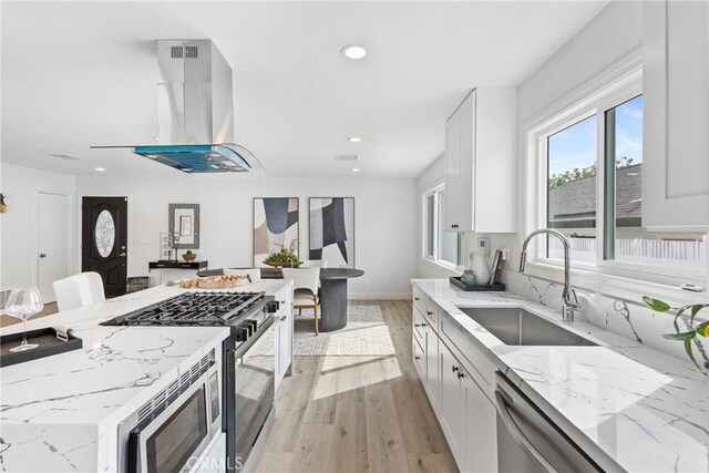 kitchen featuring white cabinetry, island exhaust hood, sink, and light stone counters