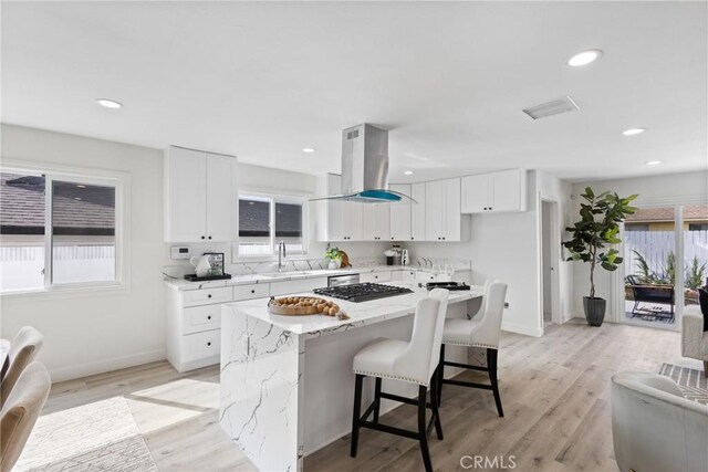 kitchen featuring sink, island range hood, stainless steel gas cooktop, white cabinets, and a kitchen island