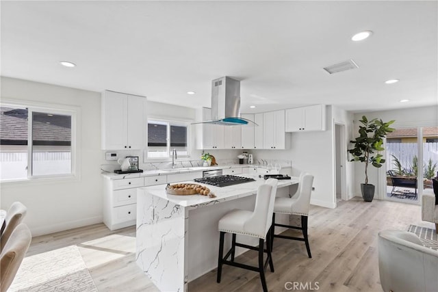 kitchen with island range hood, sink, white cabinets, a center island, and stainless steel gas cooktop