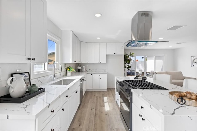 kitchen featuring light stone countertops, island range hood, white cabinets, and black gas range