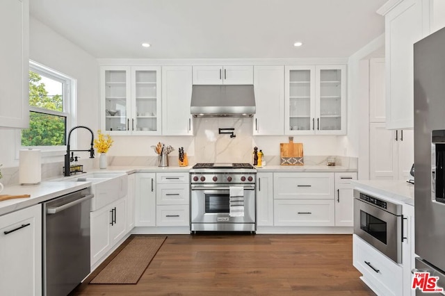 kitchen with appliances with stainless steel finishes, dark hardwood / wood-style floors, ventilation hood, sink, and white cabinets