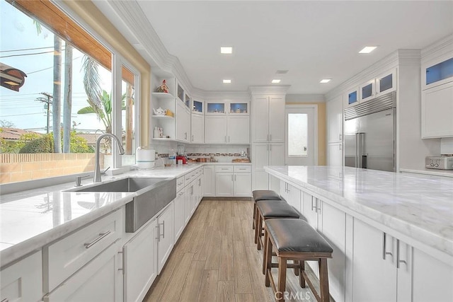 kitchen with light stone counters, white cabinets, and built in refrigerator