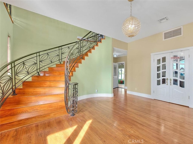 stairway with french doors, wood-type flooring, and a notable chandelier