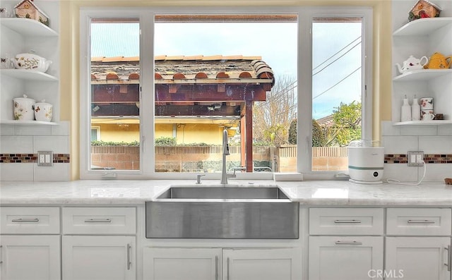 kitchen featuring white cabinets, sink, backsplash, and light stone counters