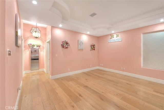 empty room featuring light wood-type flooring and a tray ceiling