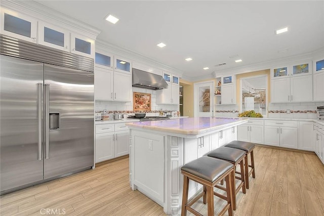 kitchen with a kitchen island, appliances with stainless steel finishes, white cabinets, and wall chimney exhaust hood