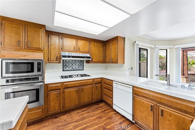 kitchen with sink, tile counters, hardwood / wood-style floors, and appliances with stainless steel finishes