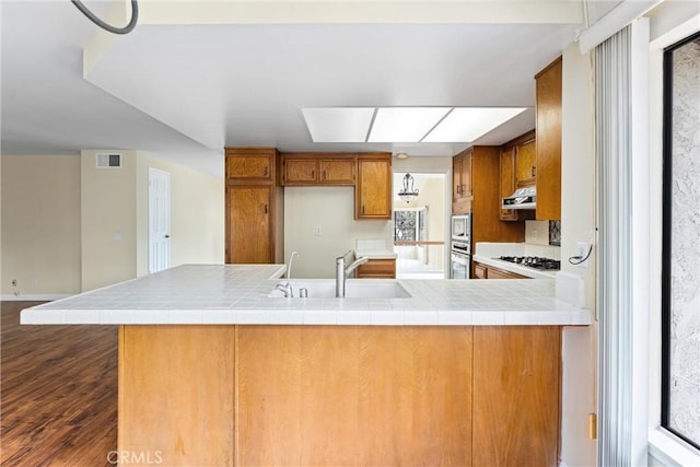 kitchen with sink, gas stovetop, tile counters, dark hardwood / wood-style floors, and kitchen peninsula