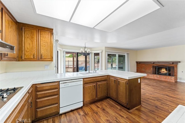 kitchen featuring dark wood-type flooring, gas stovetop, a brick fireplace, white dishwasher, and kitchen peninsula