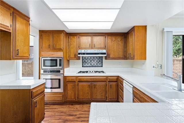 kitchen featuring sink, appliances with stainless steel finishes, tile counters, dark hardwood / wood-style flooring, and kitchen peninsula